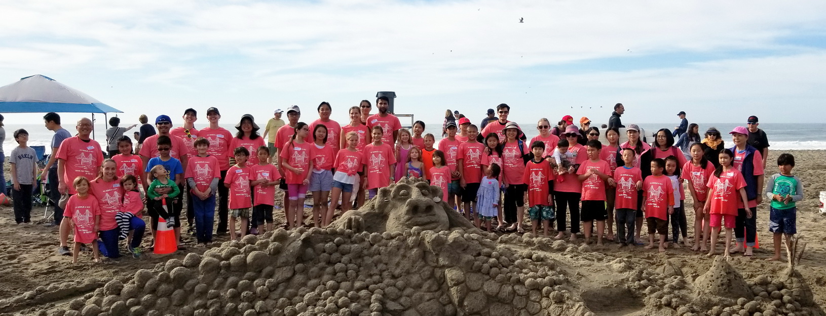 A big group of students standing in front of a sand castle at Ocean Beach